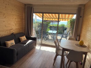 Ein Zimmer mit einer Couch, einem Esstisch und Stühlen, einer Glastür mit Schiebeöffnung zu einem Außenbereich mit Tisch und Stühlen sowie einem gelben Paprika auf dem Tisch.