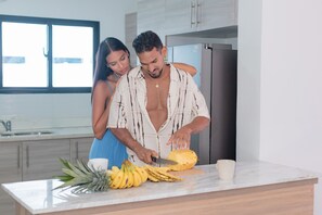 A modern kitchen with a large window, a countertop with fruits, and a refrigerator. - Luxury 4BR Punta Cana Villa | Private Pool & Beach Access (Punta Cana)