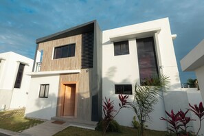 Ein modernes, zweistöckiges Haus mit Flachdach, großen Fenstern und einer sichtbaren Tür.