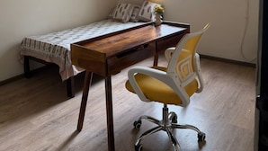 A small room with a bed, a desk, a chair, a ceiling fan, a window with curtains, and an air conditioner. - Beautiful 3-bedroom apartment with AC in cool Noida neighborhood (Noida)