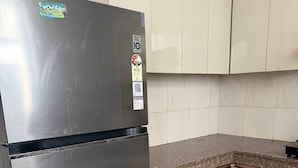 A kitchen with a stainless steel refrigerator, beige cabinets, and a granite countertop. - Beautiful 3-bedroom apartment with AC in cool Noida neighborhood (Noida)
