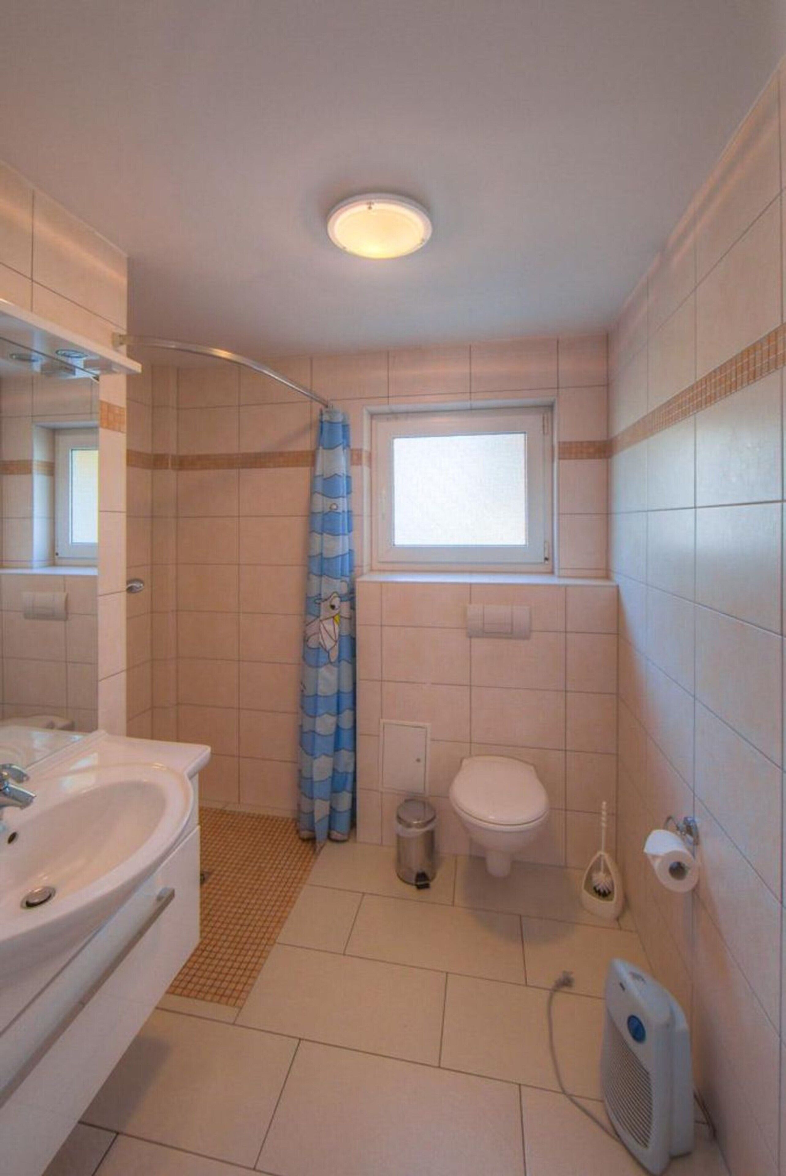 Une salle de bain avec un lavabo, des toilettes, un rideau de douche et une fenêtre.