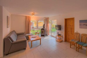 Ein Wohnzimmer mit einer Couch, einem Tisch, einem Fernseher, einem Kamin und einer Tür, die nach draußen führt.