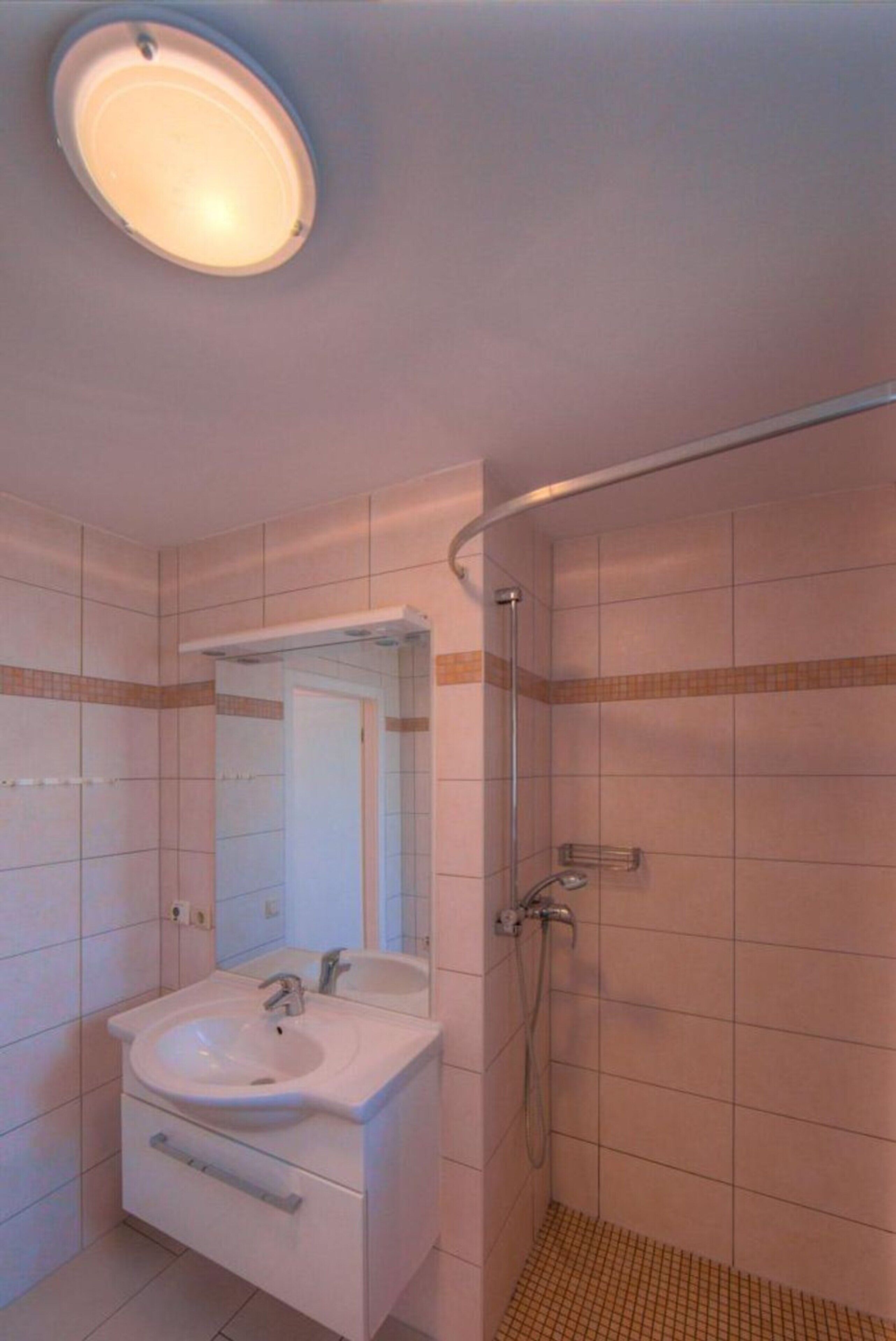 Ein Badezimmer mit einem weißen Waschbecken, einem Spiegel und einer Duschkabine.