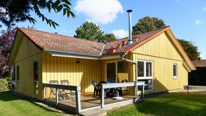 A yellow wooden house with a tiled roof, a porch with chairs, and a chimney. - Komfortabler Doppelbungalow mit Terrasse im Ferienpark Mirow (Mirow)