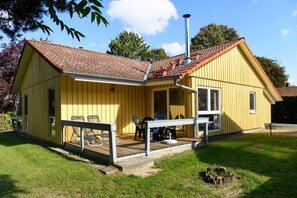 Ein gelbes Holzhaus mit einem Ziegeldach, einer Veranda mit Stühlen und einem Schornstein.