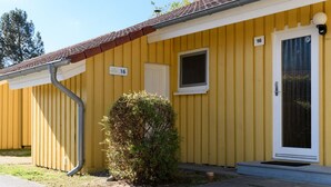 A yellow building with a white door and window, number 16, and a small bush in front. - Komfortabler Doppelbungalow mit Terrasse im Ferienpark Mirow (Mirow)