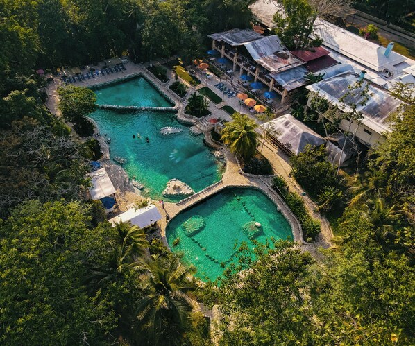 An aerial view of a resort with multiple swimming pools surrounded by lush greenery, a bar area, and a restaurant.