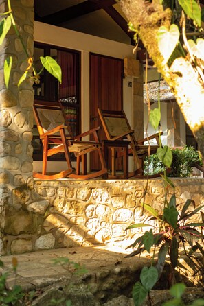 A stone wall with two wooden rocking chairs facing a building with a window and a door.