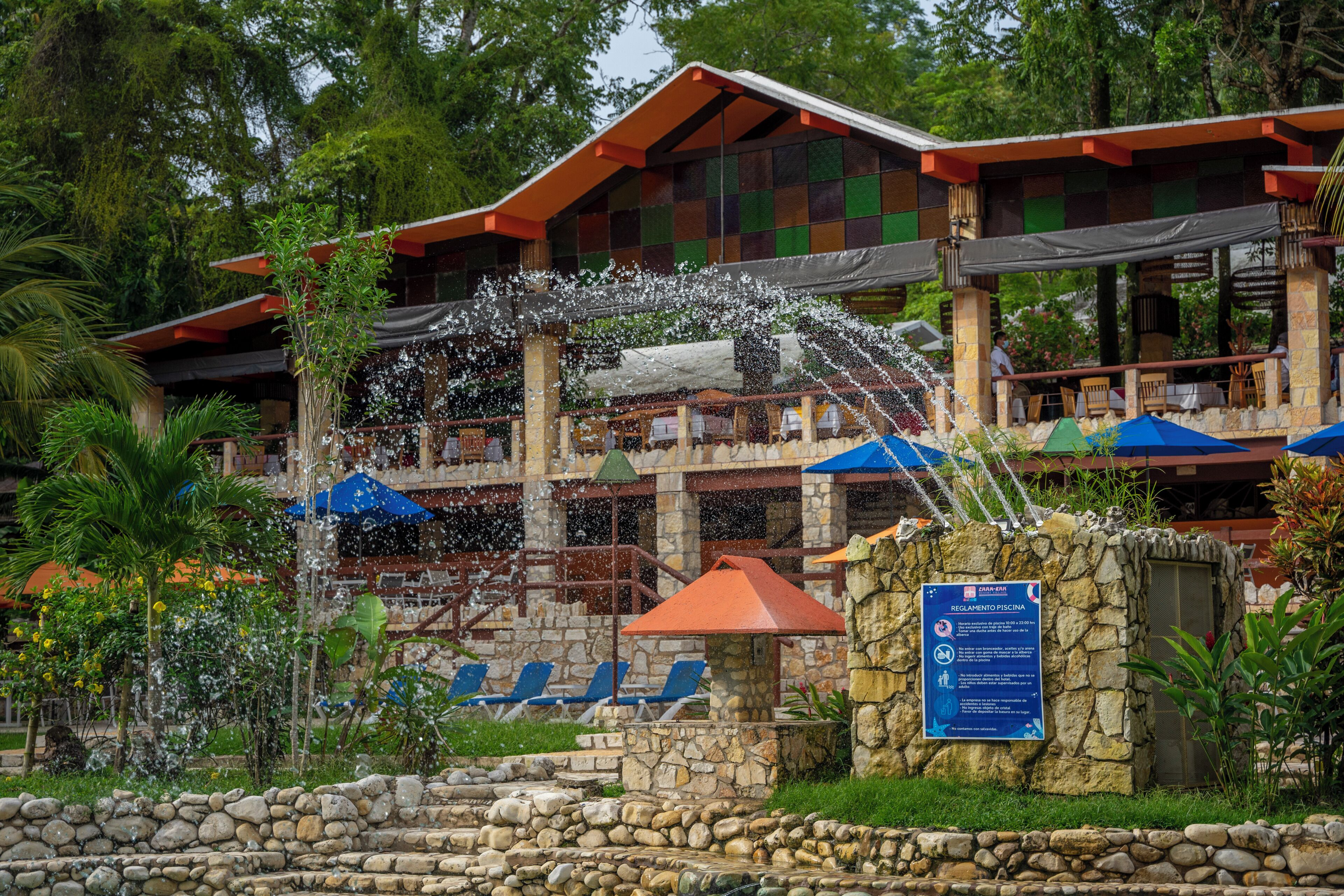 A hotel with a stone facade, outdoor seating, and a water feature.