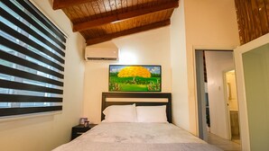 Un dormitorio con cama, un cuadro de un árbol, una ventana con persianas y un equipo de aire acondicionado.