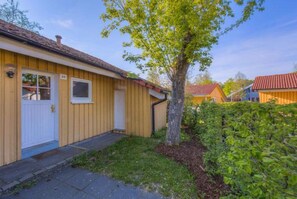 Ein eingeschossiges Holzhaus mit einer weißen Tür, einem kleinen Fenster und einem Baum davor.