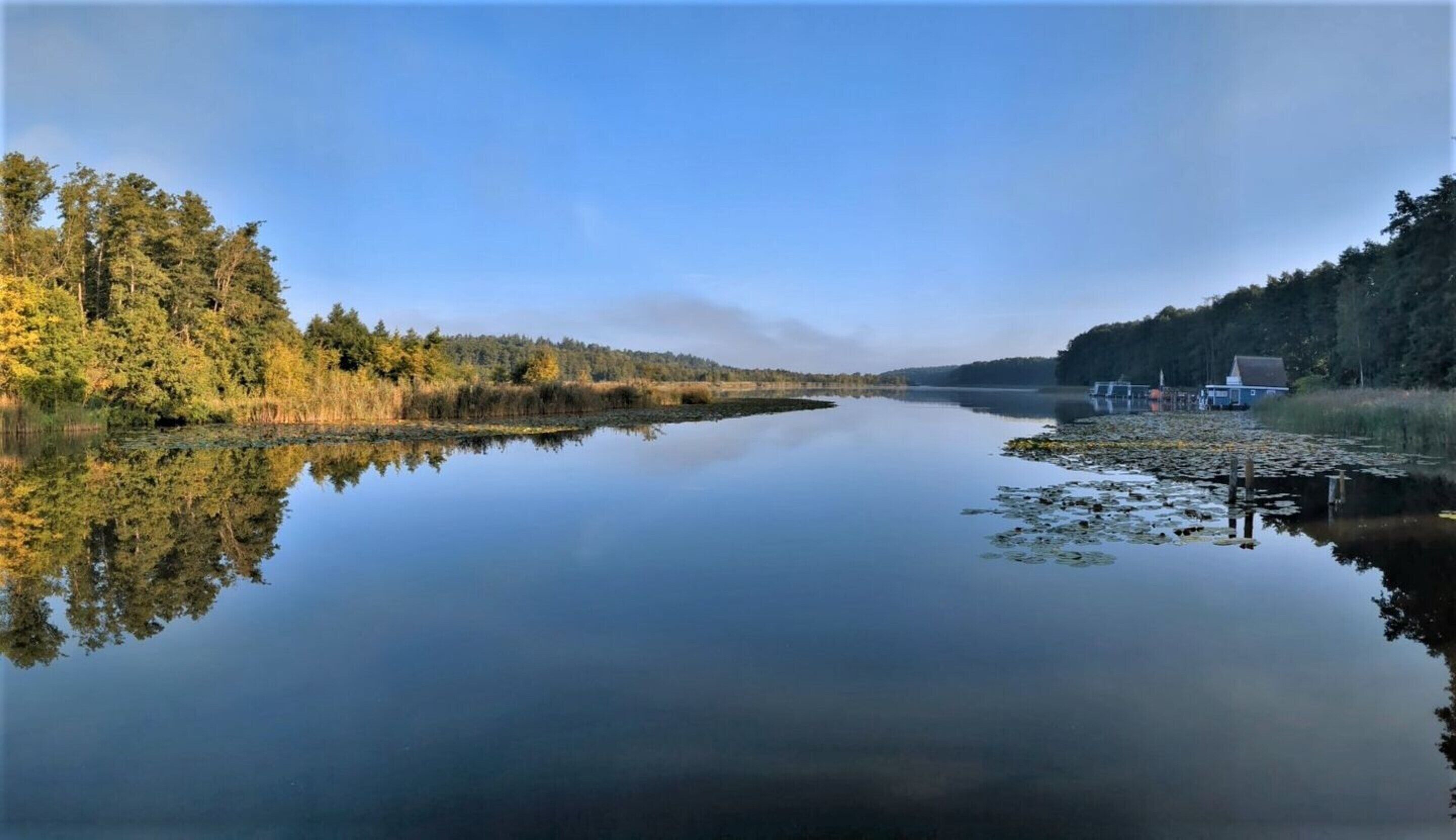 Un lac paisible, avec un quai et une maison sur la droite.