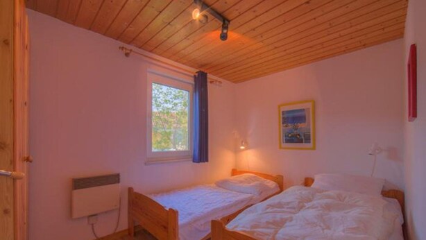 Ett rum med två sängar av trä, ett fönster, ett element och en tavla på väggen.