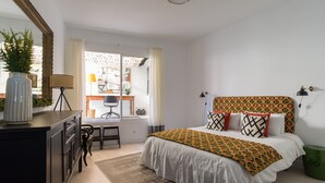 A bedroom with a bed, a desk, a chair, a dresser, and a window with curtains. - Townhouse in Las Palmas Near Playa Alcaravaneras (Las Palmas de Gran Canaria)
