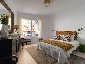A bedroom with a bed, a desk, a chair, a dresser, and a window with curtains. - Townhouse in Las Palmas Near Playa Alcaravaneras (Las Palmas de Gran Canaria)