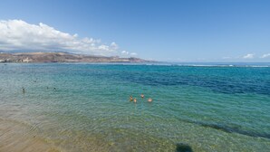 A beach with clear water and a distant view of hills. - Townhouse in Las Palmas Near Playa Alcaravaneras (Las Palmas de Gran Canaria)