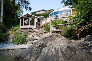A wooden cabin with a deck, surrounded by rocks and vegetation.