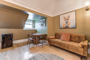 Ein Wohnzimmer mit braunem Sofa, einem Esstisch mit Stühlen, einem schwarzen Kühlschrank und einem Fox-Gemälde an der Wand.