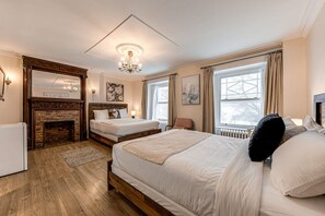 A bedroom with two beds, a fireplace, a chandelier, and large windows. - Auberge in Old Quebec -2 bed suite (Québec)