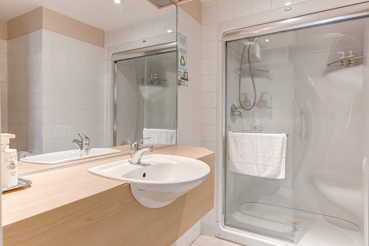 Une salle de bain moderne avec deux vasques, une douche à l’italienne en verre et un grand miroir.