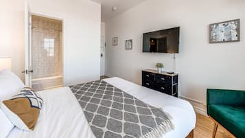 Ein Schlafzimmer mit einem Bett, einem Schminktisch, einem Fernseher und einem grünen Sessel.