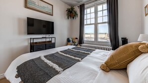 A hotel room with a bed, a TV, a window with curtains, a plant, and a view of the city.