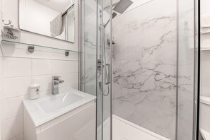 Une salle de bain moderne avec une douche en verre, un lavabo blanc et un mur recouvert de carreaux de marbre.