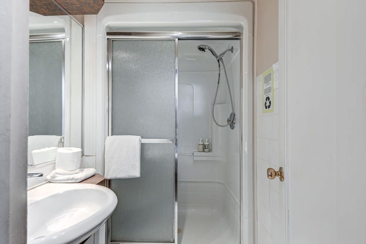 A bathroom with a white sink, a glass shower enclosure, and a towel hanging on the door.