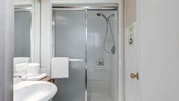 A bathroom with a white sink, a glass shower enclosure, and a towel hanging on the door.