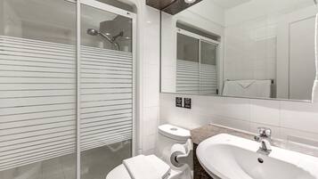 A modern bathroom with a glass-enclosed shower, a white toilet, a sink, and a large mirror.