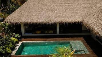 A poolside area with a thatched-roof structure, a clear pool, and lounge chairs.