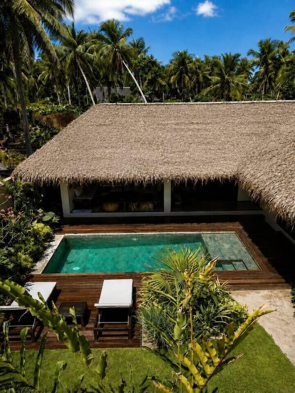 A poolside area with a thatched-roof structure, a clear pool, and lounge chairs.
