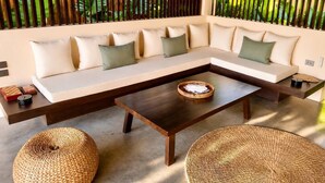 Un salon moderne avec un canapé d’angle, une table basse en bois et des poufs en fibres tressées.