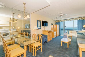 A hotel room with a dining table, chairs, a sofa, a TV, a ceiling fan, and a view of the ocean. - Oceanfront Stay by Skywheel! Yachtsman 1002 (Myrtle Beach)
