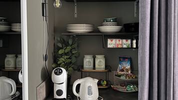 Une petite cuisine équipée d’une machine à café, d’une bouilloire et d’étagères pour ranger la vaisselle et les bocaux.