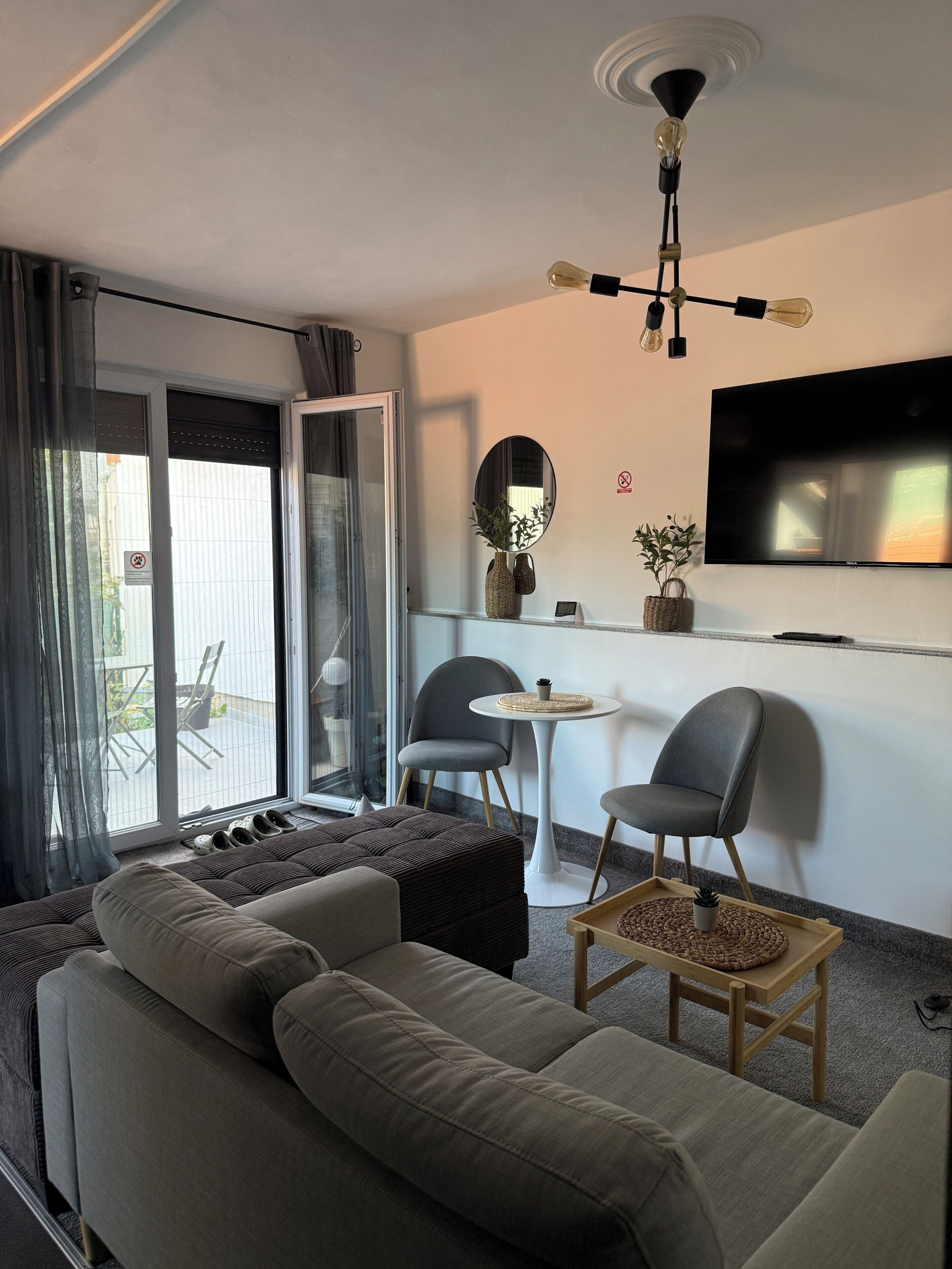 A modern living room with a sofa, chairs, a small table, and a TV mounted on the wall.