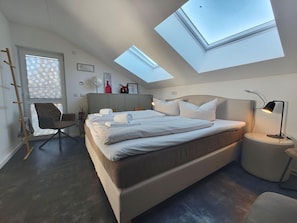 A modern bedroom with a skylight, a bed, a chair, and a bedside table. - Modernes Apartment mit Blick auf den Hafen in Rechlin (Rechlin)