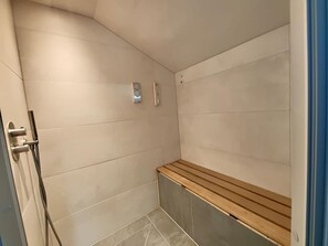 Un espacio de ducha con un banco, un reloj en la pared y un perchero para toallas.