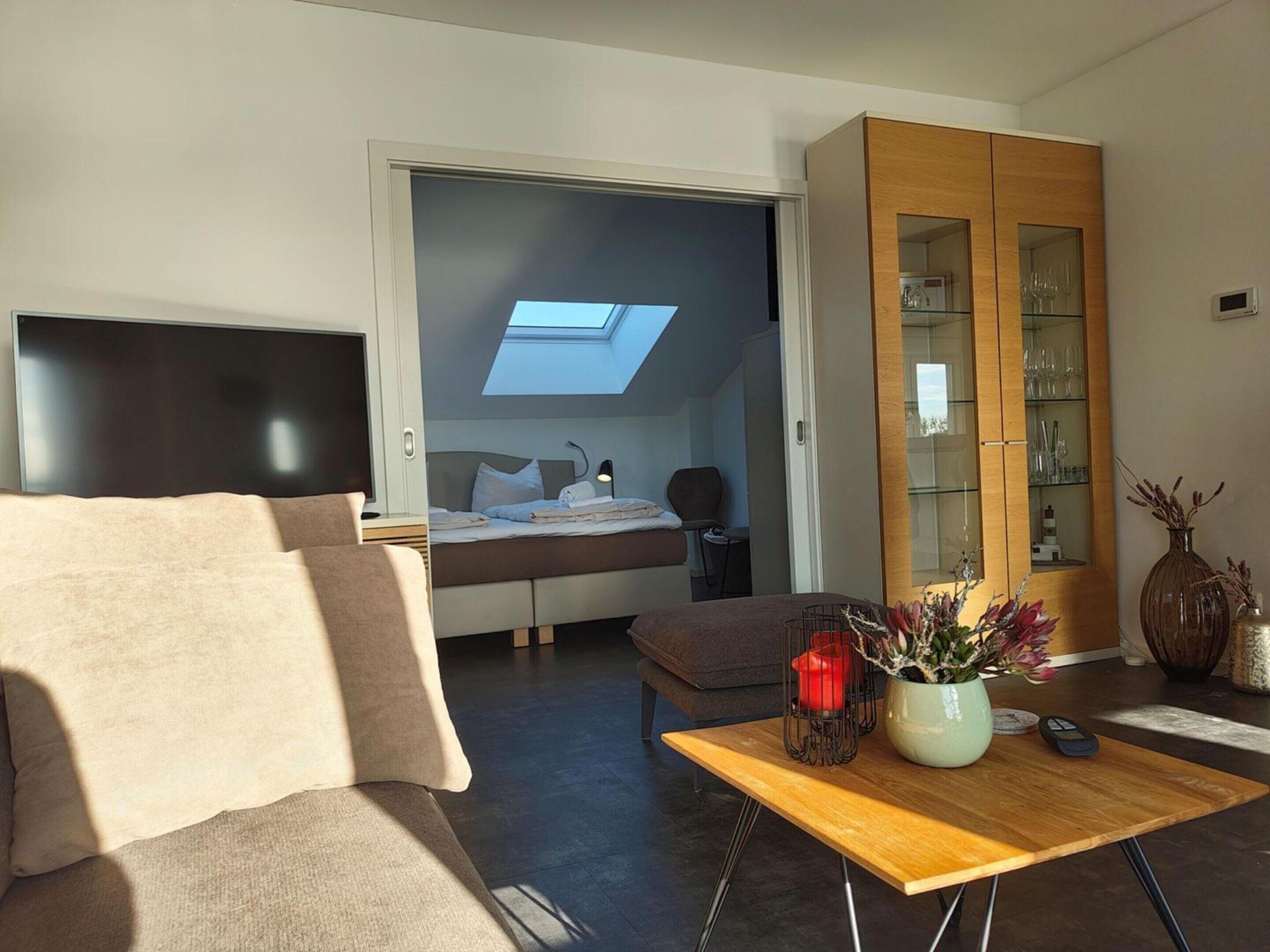 A modern bedroom with a skylight, a bed, a bedside table, and a wooden cabinet with glass doors.