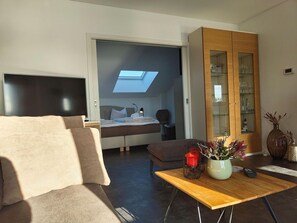 A modern bedroom with a skylight, a bed, a bedside table, and a wooden cabinet with glass doors. - Modernes Apartment mit Blick auf den Hafen in Rechlin (Rechlin)