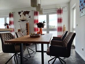 A dining area with a wooden table, cushioned chairs, a world map, and a sailboat decoration. - Modernes Apartment mit Blick auf den Hafen in Rechlin (Rechlin)