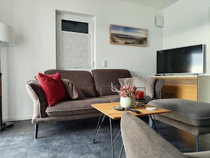 A modern living room with a sofa, a coffee table, a TV, and a painting on the wall. - Modernes Apartment mit Blick auf den Hafen in Rechlin (Rechlin)