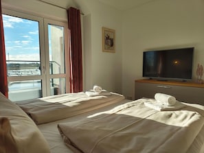 Habitación de hotel con dos camas, televisión y ventana con cortinas.