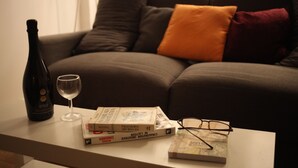 Un salon avec un canapé, une table sur laquelle se trouvent une bouteille, un verre, des livres et des lunettes.