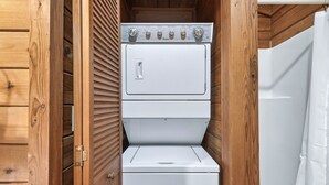 A compact laundry room with a stacked washer and dryer, wooden walls, and a shower curtain. - Hot Tub + King Bed +1.4 Miles from Parkway (Sevierville)