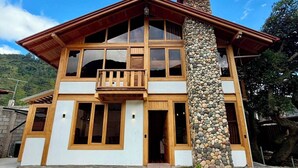 Una casa de dos pisos con un pilar de piedra, ventanas grandes y un balcón.