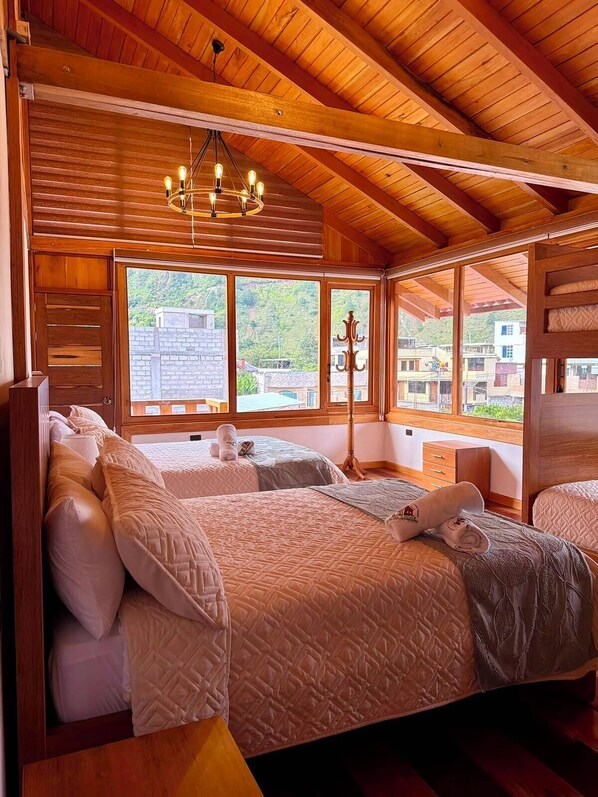 Una habitación con paneles de madera, dos camas, una araña y ventanas amplias con vistas a una colina.