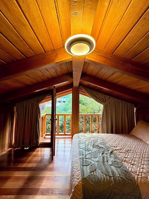 Un dormitorio con techo de madera, cama con colcha estampada y vistas a la vegetación.