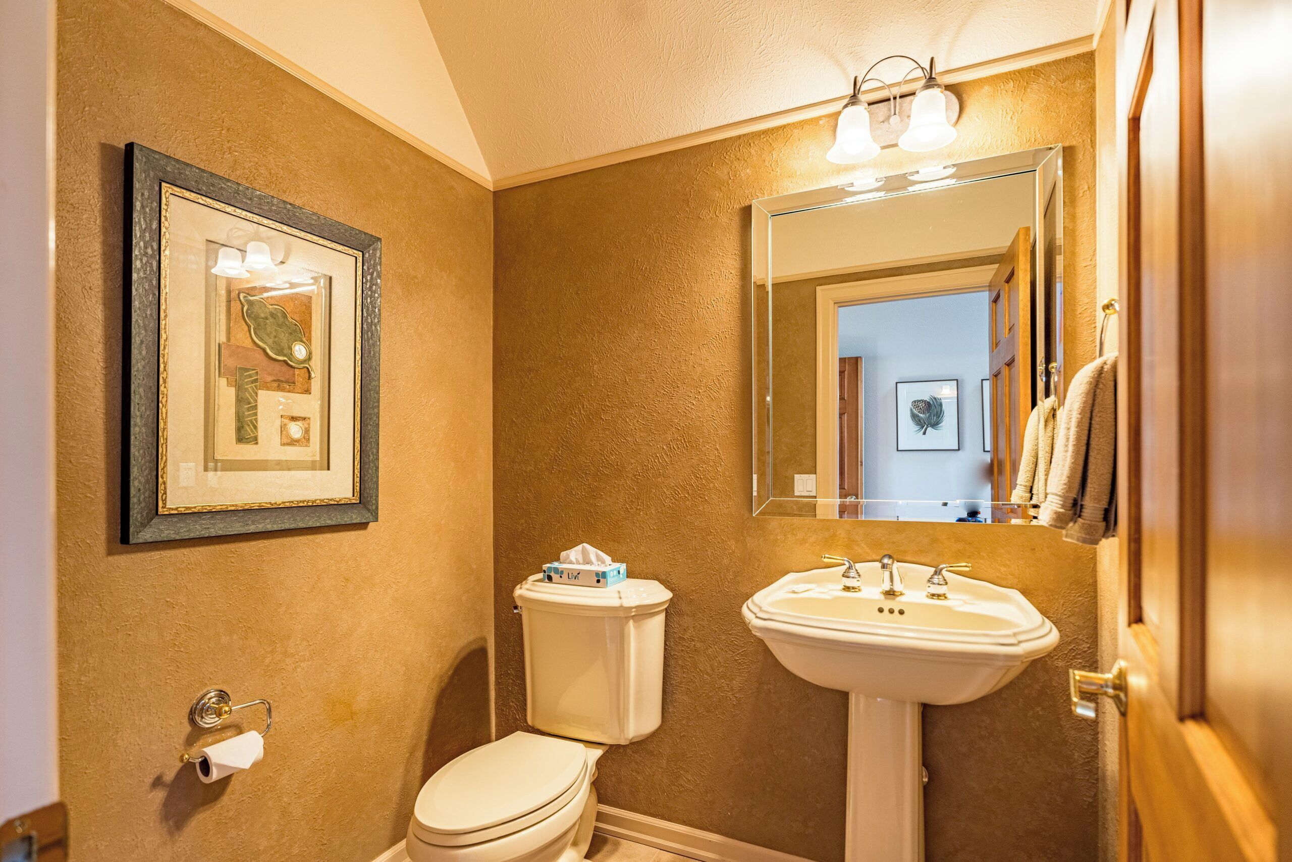 A bathroom with a toilet, sink, framed artwork, and a mirror.
